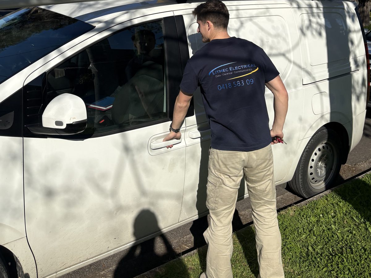Litmec electrician at the door of the company work van, Litmec Electrical branding across the back of his shirt